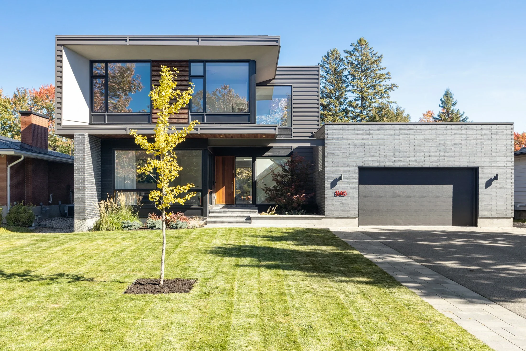 A modern home with a young tree, green lawn, and paved driveway
