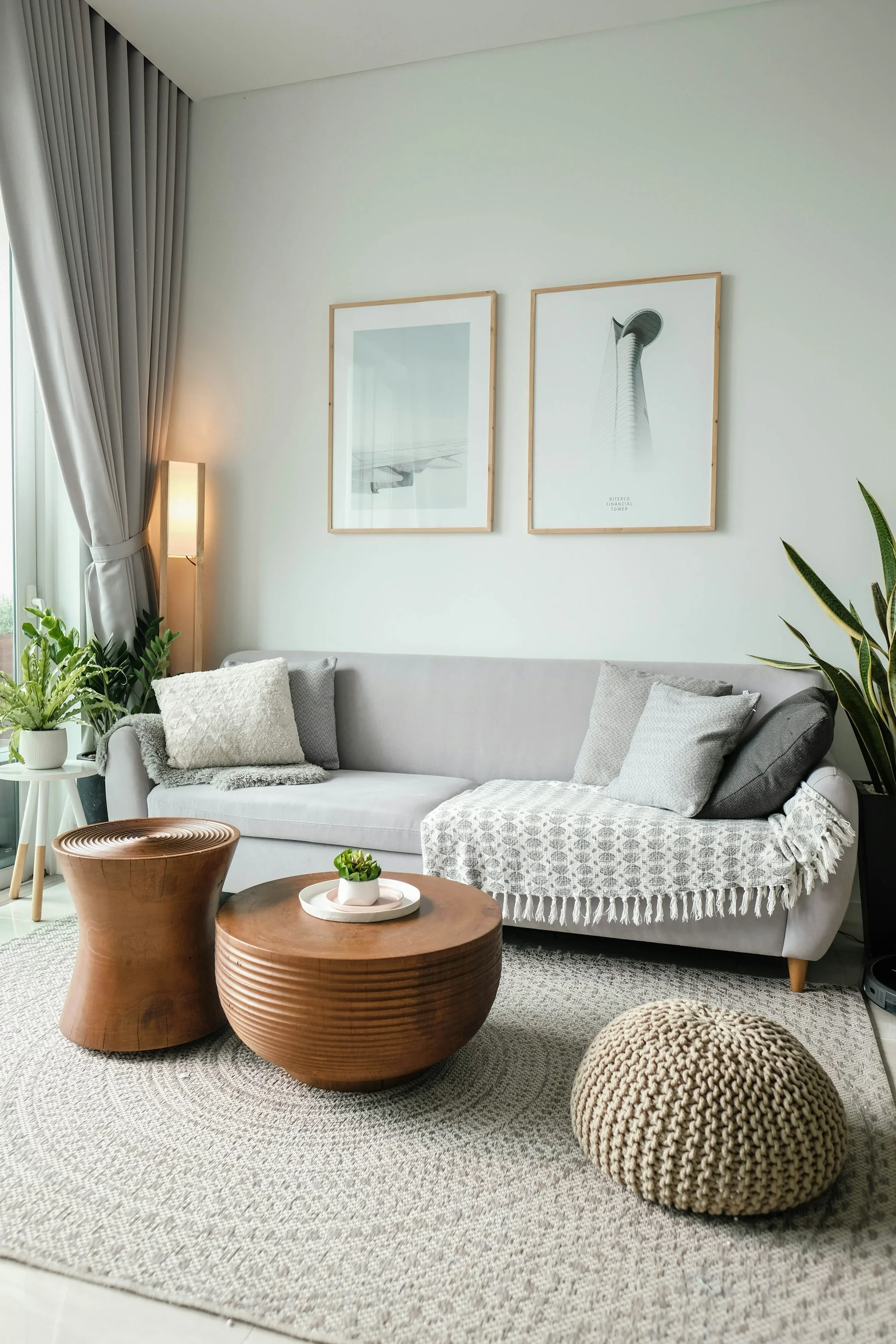 A bright living room with a neutral sofa, plants, and natural window light